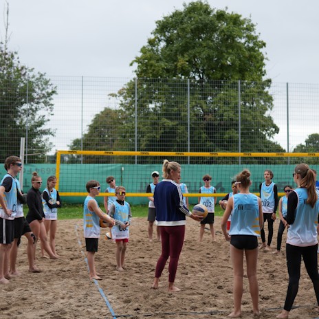 Profi Volleyballerin erklärt den Beach Camp Teilnehmern etwas auf dem Beach Feld