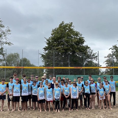 Gruppenbild Beach Camp auf dem Beach Volleypla Feld vor dem Netz. Alle Teilnehmer tragen hellblaue tops