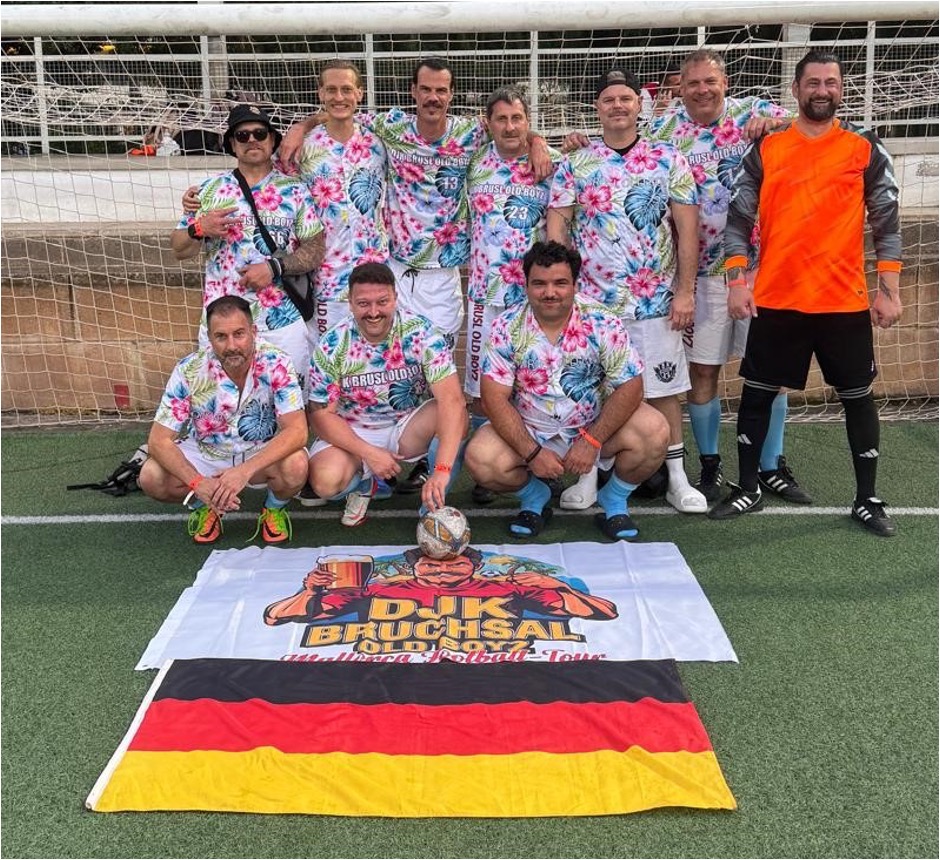 Mannschaftsfoto der DJK Bruchsal Old Boyz bei der Mallorca Football Tour. Die Spieler posieren in bunten Hawaiihemden vor einem Fußballtor. Im Vordergrund liegen ein Fußball sowie eine Banner mit dem Gruppenlogo und die deutsche Flagge.