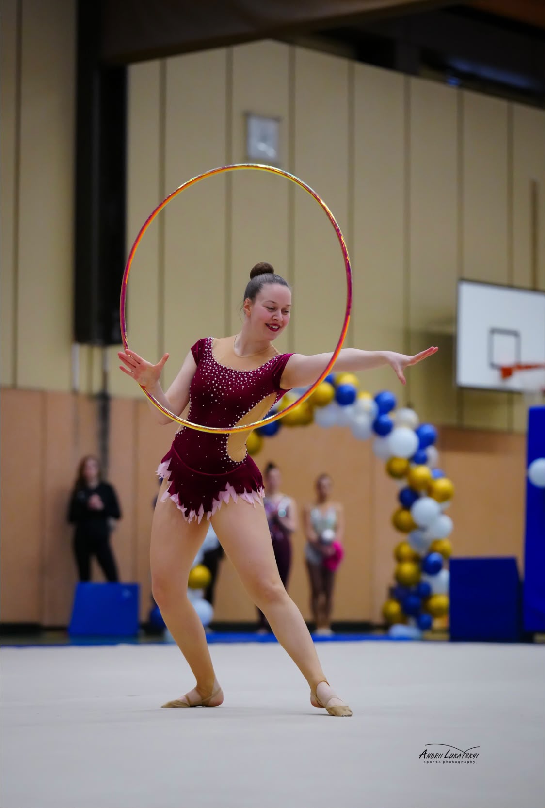 Gymnastin in weintotem Anzug bei ihrer Reifenkür in einer Turnhalle.