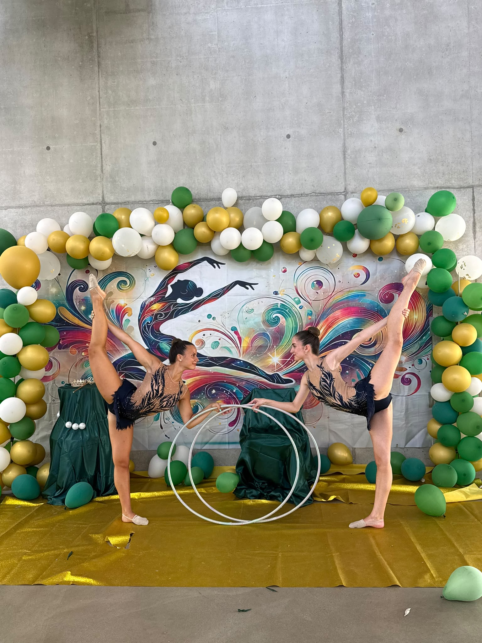 Zwei Gymnastinnen im Penché Stand vor bunter Fotowand und Ballonbogen.